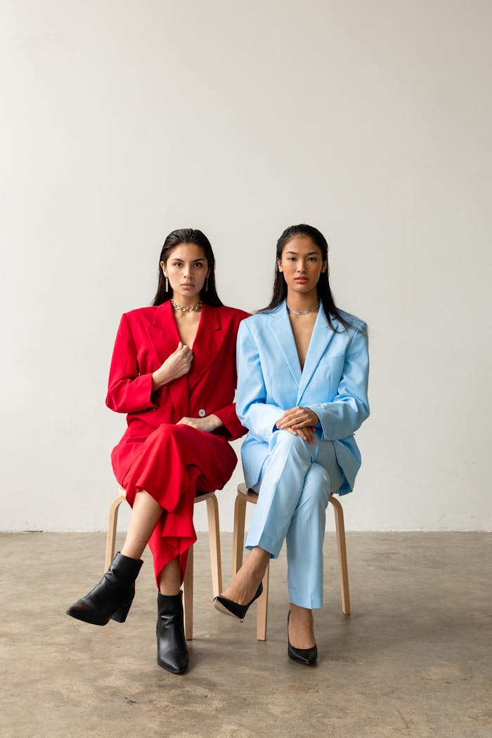 Two women elegantly pose in striking red and blue suits. Perfect for fashion editorials.